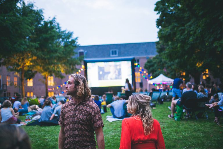 Zittend of liggend in het gras kijken bezoekers naar de film tijdens Movies @ H'ART Museum.