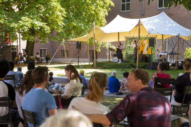 Bezoekers zitten in de binnentuin en luisteren naar een jazz band.