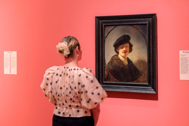 Een jonge blonde vrouw kijkt naar het zelfportret van Rembrandt van Rijn