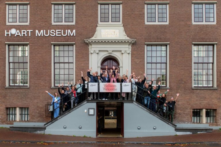 Groepsfoto van H'ART Museum medewerkers aan de ingang van het museum
